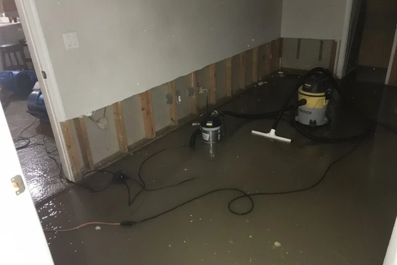 Extraction equipment pulling floodwater from a room with the drywall cut away