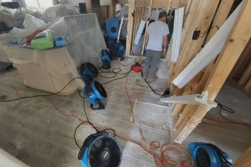 Air movers drying a room with an open wall stud bay during water damage repair in a Baldwin, NY home