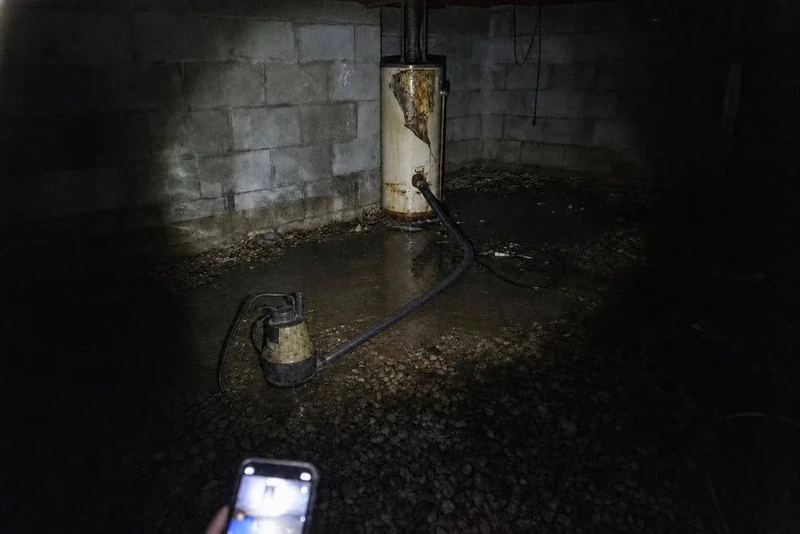 Submersible pump draining a flooded crawl space beside a corroded water heater in a Baldwin, NY home